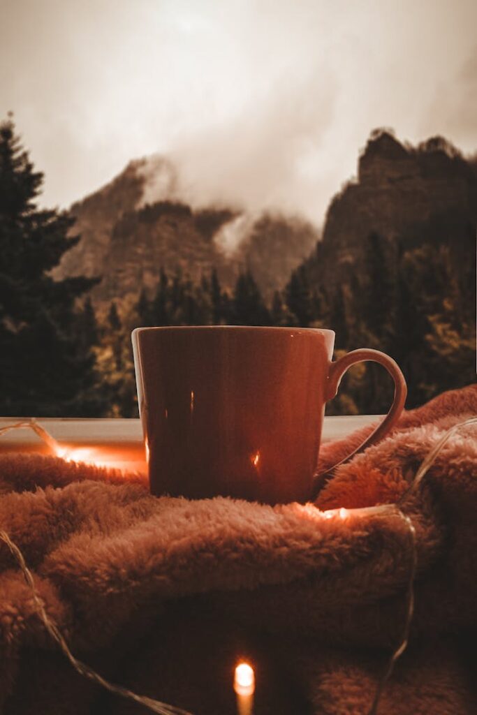 Cozy plaid with mug of warming beverage in garland lights with view of misty mountains