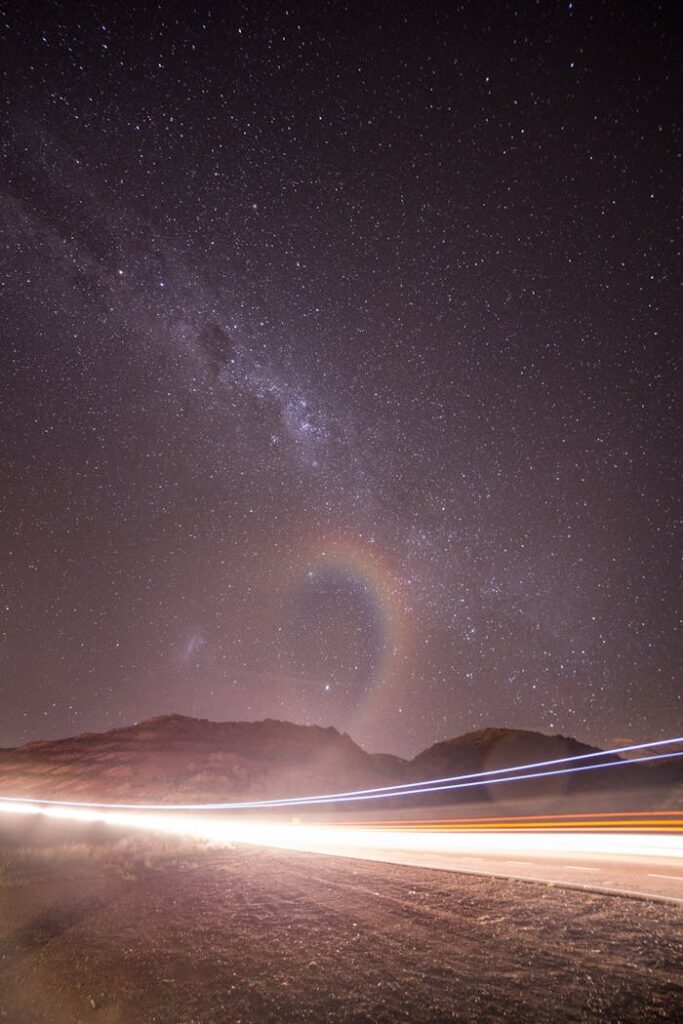 Long exposure magnificent scenery of starry night sky over mountainous roadway running through rocky terrain